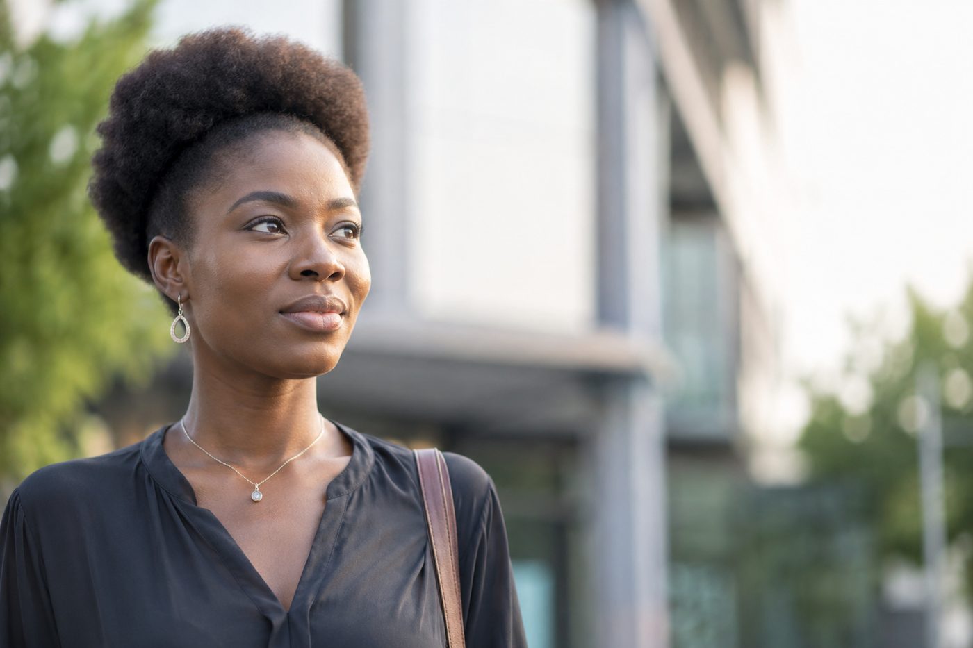 Une femme regarde au loin, dans la lumiere naturelle, devant un batiment en ville.